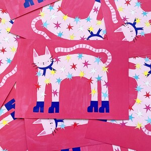 May include: Pink cards featuring a white cat illustration adorned with colorful star cutouts. The cat has a blue scarf and blue boots. The background is a solid pink color.