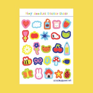 May include: A sticker sheet with the text "tiny doodles Sticker Sheet" features colorful, hand-drawn illustrations. Designs include a heart, cloud, apple, toast, strawberry, flower, star, cat face, cherry, pencil, bee, bow, mushroom, cup, butterfly, bunny, house, star, and ladybug.