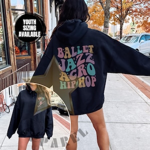 Peut inclure: Sweat-shirt à capuche noir avec les mots "Ballet Jazz Acro Hip Hop" en police rétro colorée au dos. Le sweat-shirt est porté par une personne.