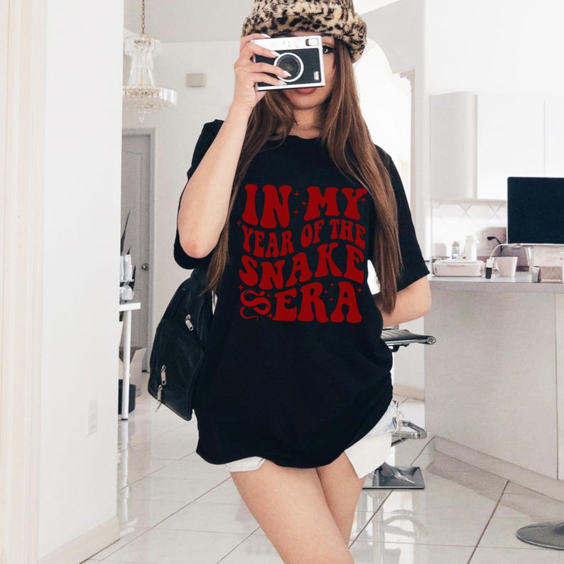 May include: A black t-shirt with a red graphic that says "In My Year of the Snake Era".