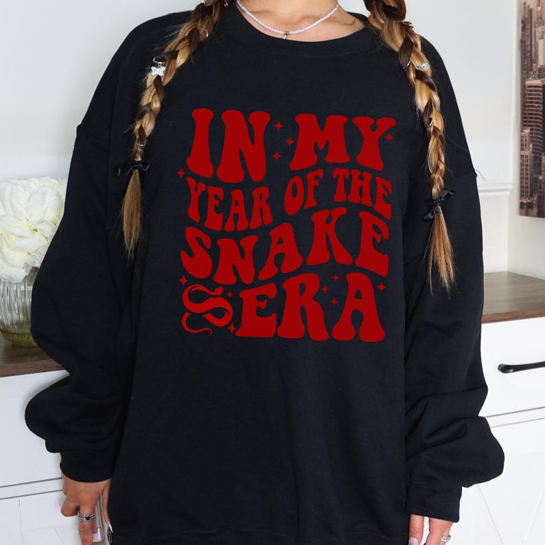 May include: Black sweatshirt with red text that reads "In My Year of the Snake Era" with a snake graphic.