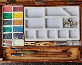 May include: A wooden watercolor paint box with a white plastic tray, 12 paint pans, 3 paintbrushes, 2 clothespins, a small spray bottle, and the text "Irisvana Creations".