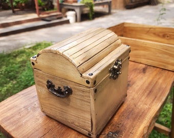 May include: A small wooden chest with a hinged lid, a metal handle, and a metal latch. The chest is painted a light brown color and has a distressed finish.
