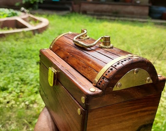 May include: A wooden box with a brass latch and handle. The box has a dark brown finish and is decorated with brass accents.