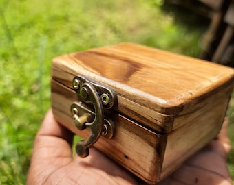 May include: A small wooden box with a brass latch. The box is made of light and dark wood and has a natural finish.