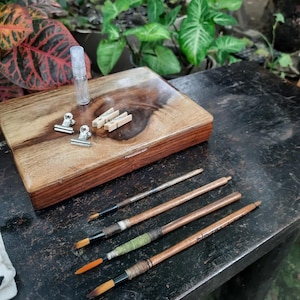May include: A wooden box with a lid, two silver clips, three wooden clothespins, a small clear bottle, and four paintbrushes with wooden handles and colorful wrappings.