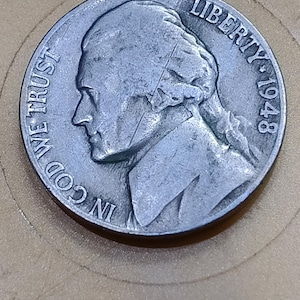 May include: A silver-colored United States five-cent coin featuring a profile portrait of Thomas Jefferson facing left. The text IN GOD WE TRUST is inscribed on the left side, and the word LIBERTY followed by the year 1948 is on the right side.