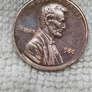 May include: A copper-coloured United States one-cent coin featuring a profile portrait of Abraham Lincoln facing right. The text IN GOD WE TRUST is arched along the top, the word LIBERTY is on the left, and the year 1988 is printed on the right.