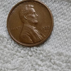 May include: A copper-coloured United States one-cent coin featuring the profile of Abraham Lincoln facing right. The coin is inscribed with the text IN GOD WE TRUST, LIBERTY, and the year 1972 with a D mint mark located below the date.