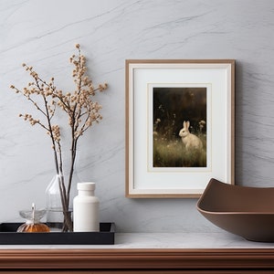 May include: A framed print of a white rabbit sitting in a field of wildflowers. The print is in a light wood frame with a white mat.
