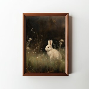 May include: A white rabbit sits in a field of green grass and white flowers. The background is dark and blurry, creating a sense of depth. The rabbit's fur is soft and fluffy, and its eyes are bright and alert.