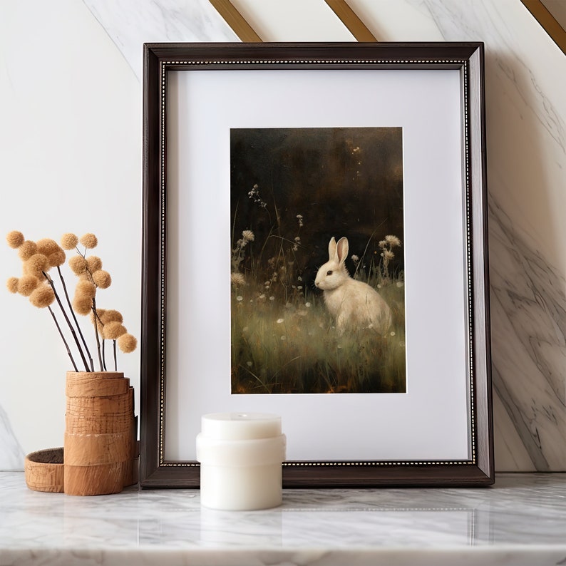 May include: A framed print of a white rabbit sitting in a field of green grass and white flowers. The rabbit is looking to the left of the image. The background is dark and blurry.