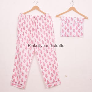 May include: White pajama set with a repeating pink floral pattern. The set includes trousers and a matching pouch, all hanging on wooden hangers. The text "Pinkcityhandicrafts" is visible on the trousers.