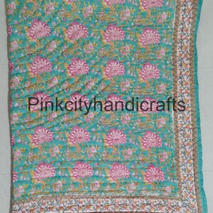 Puede incluir: Una colcha de algod&oacute;n azul turquesa con un patr&oacute;n floral en tonos de rosa y verde. La colcha tiene un borde blanco con un patr&oacute;n geom&eacute;trico gris y blanco.