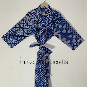 May include: A blue and white cotton robe with a patchwork design. The robe has a tie belt and long sleeves. The fabric features various geometric patterns, including circles, swirls, and leaves.
