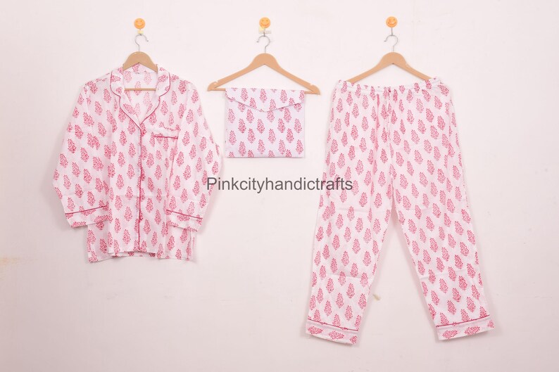 May include: A white pajama set with a pink leaf pattern, comprising a button-down shirt, trousers, and a matching pouch. The set is displayed on wooden hangers against a plain white background. The text "Pinkcityhandicrafts" is visible.