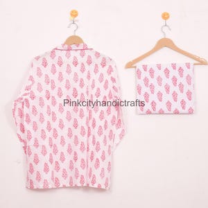 May include: White pajama set with a red floral pattern, including a long-sleeved top and matching folded bottoms, hanging on wooden hangers. The top has a collared neckline. The text "Pinkcityhandicrafts" is visible.
