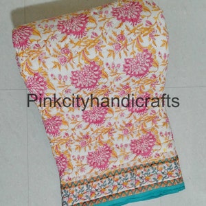 Puede incluir: Una colcha de algod&oacute;n blanco con estampado floral en tonos rosa y amarillo. La colcha tiene un borde turquesa con un patr&oacute;n floral blanco y amarillo. La colcha est&aacute; doblada y enrollada, y el texto "Pinkcityhandicrafts" es visible en el centro de la imagen.