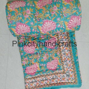 Puede incluir: Una colcha de algod&oacute;n azul turquesa con estampado floral en tonos rosa, amarillo y verde. La colcha tiene un borde con un patr&oacute;n geom&eacute;trico en blanco, gris y naranja.