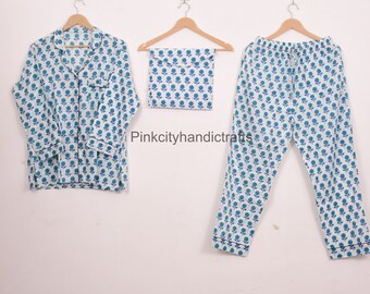 May include: A three-piece pyjama set with a white backdrop and a repeating blue floral design. The set includes a button-down shirt, drawstring trousers, and a matching pouch. The pyjamas are displayed on wooden hangers.