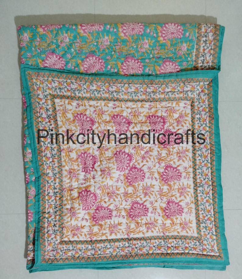Puede incluir: Una colcha de color azul turquesa y blanco con estampado floral, con una colcha interior m&aacute;s peque&ntilde;a con estampado floral rosa y blanco. La colcha tiene un borde decorativo con un patr&oacute;n repetitivo de tri&aacute;ngulos. El texto "Pinkcityhandicrafts" es visible en el centro de la colcha.