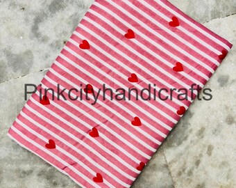May include: A folded fabric with a pink and white striped pattern, adorned with scattered red heart shapes. The text "Pinkcityhandicrafts" is printed on the fabric. The fabric is likely used for crafting or sewing projects.