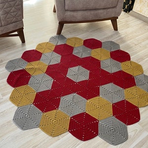 Könnte beinhalten: Ein gehäkelter Teppich mit einem sechseckigen Muster in Rot-, Grau- und Gelbtönen.