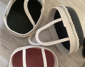 May include: Three oval-shaped rope baskets with white rope handles. The baskets are lined with fabric in black, pink, and white.