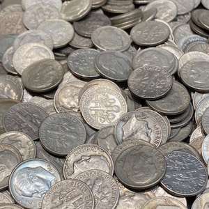 May include: A large collection of silver-coloured US dimes. The coins are arranged in a random pattern and some are stacked on top of each other. The coins feature the words "United States of America" and "One Dime" along with the image of Lady Liberty.