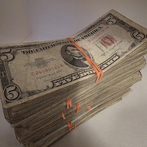 May include: A white ceramic mug with a black handle and the text "But First, Coffee" in a bold, black font. The mug is set against a blurred background, suggesting a cozy setting.