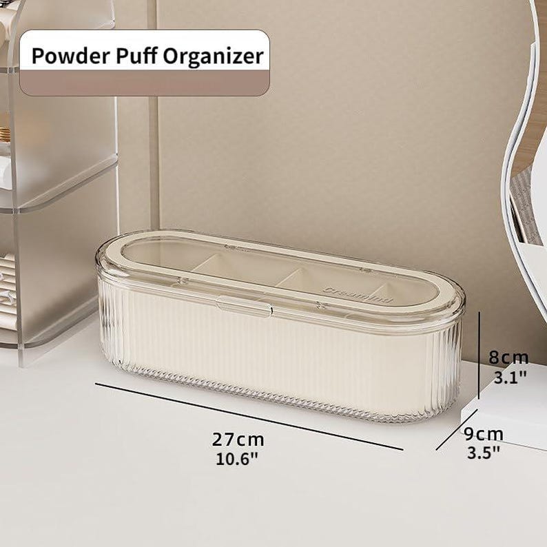 May include: A clear, ribbed powder puff organizer with a clear lid. The organizer is rectangular, measuring 10.6 inches long, 3.5 inches wide, and 3.1 inches high. The text "Powder Puff Organizer" is displayed on the top.