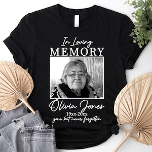 May include: Black t-shirt with the text "In Loving Memory" above a black and white photo of a woman. The name "Olivia Jones" and dates are below the photo, with the phrase "gone but never forgotten".