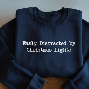 May include: Navy blue sweatshirt with the text "Easly Distracted by Christmas Lights" in white. The text is in a typewriter-style font. The sweatshirt has a crew neck and long sleeves.