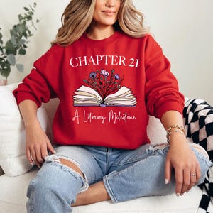 a woman sitting on a couch wearing a red sweatshirt