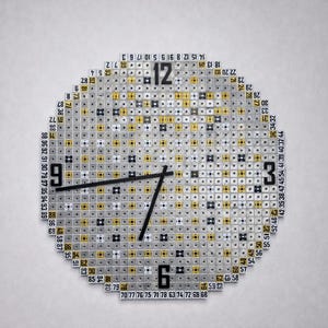 Op de afbeelding: Een unieke, ronde wandklok met een gepixeld ontwerp. De wijzerplaat bestaat uit kleine, vierkante tegels in zilver, geel en zwart. Zwarte wijzers geven de tijd aan. Cijfers staan rond de rand van de wijzerplaat.