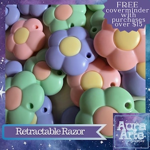 May include: A selection of pastel-coloured flower-shaped retractable razors. The razors are in shades of pink, green, and purple with yellow and peach centres. The image includes text that reads "Retractable Razor" and "FREE coverminder with purchases over £15."