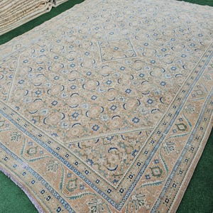 Puede incluir: Gran alfombra beige y azul con un intrincado dise&ntilde;o geom&eacute;trico. La alfombra presenta un dise&ntilde;o cuadrado central y un borde detallado con motivos florales y geom&eacute;tricos. La paleta de colores incluye beige, azul y toques de verde y marr&oacute;n.