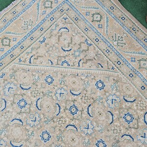 Puede incluir: Una alfombra beige y azul con un dise&ntilde;o geom&eacute;trico detallado. La alfombra presenta un campo central con motivos florales y geom&eacute;tricos repetidos en tonos azules y beige. El borde es azul oscuro con un patr&oacute;n repetitivo.