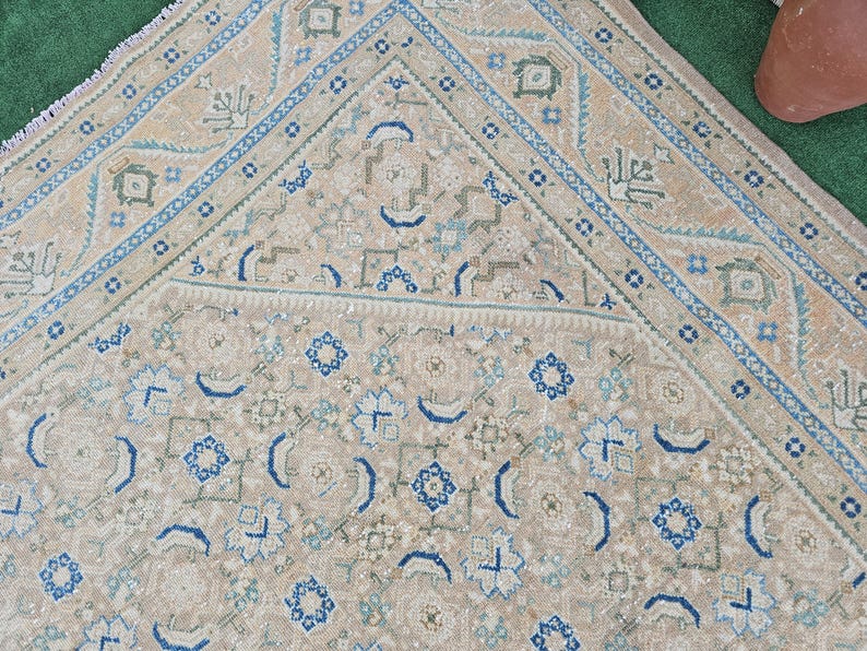 Puede incluir: Una alfombra beige y azul con un dise&ntilde;o geom&eacute;trico detallado. La alfombra presenta un campo central con motivos florales y geom&eacute;tricos repetidos en tonos azules y beige. El borde es azul oscuro con un patr&oacute;n repetitivo.