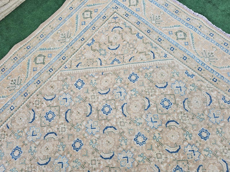 Puede incluir: Alfombra beige y azul estampada. La alfombra presenta un dise&ntilde;o geom&eacute;trico repetitivo con detalles en azul, azul claro y verde. La alfombra tiene un borde detallado y una paleta de colores suaves y neutros.