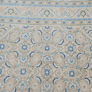 Puede incluir: Primer plano de una alfombra estampada beige y azul. La alfombra presenta un dise&ntilde;o geom&eacute;trico repetitivo con formas florales y abstractas en tonos beige, azul y verde. El borde tiene un dise&ntilde;o detallado.