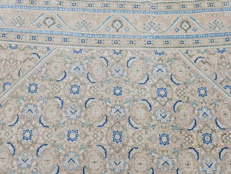 Puede incluir: Primer plano de una alfombra estampada beige y azul. La alfombra presenta un dise&ntilde;o geom&eacute;trico repetitivo con formas florales y abstractas en tonos beige, azul y verde. El borde tiene un dise&ntilde;o detallado.