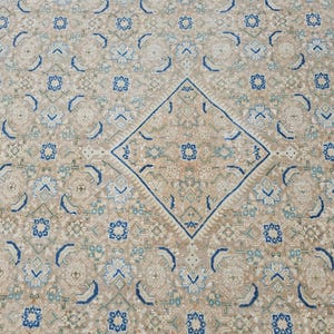 Puede incluir: Alfombra beige y azul estampada. La alfombra presenta un dise&ntilde;o central de diamante y patrones florales y geom&eacute;tricos repetidos en tonos beige, azul y verde claro. La alfombra tiene un aspecto envejecido.