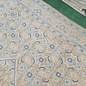 Puede incluir: Alfombra beige y azul estampada. La alfombra presenta un patr&oacute;n repetitivo de formas florales y geom&eacute;tricas en tonos beige, azul y verde. El borde tiene un dise&ntilde;o detallado con colores similares.