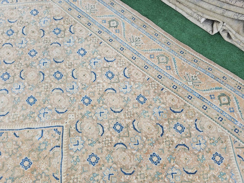 Puede incluir: Alfombra beige y azul estampada. La alfombra presenta un patr&oacute;n repetitivo de formas florales y geom&eacute;tricas en tonos beige, azul y verde. El borde tiene un dise&ntilde;o detallado con colores similares.