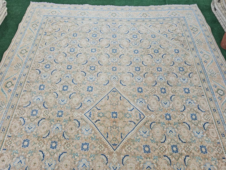 Puede incluir: Una alfombra rectangular grande con un patr&oacute;n sim&eacute;trico intrincado. La alfombra presenta un dise&ntilde;o de diamante central y motivos florales repetidos en tonos beige, azul y verde. El borde de la alfombra es de un tono beige m&aacute;s claro con patrones geom&eacute;tricos.
