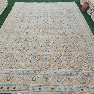 Puede incluir: Una alfombra beige rectangular grande con un intrincado patr&oacute;n de dise&ntilde;os florales y geom&eacute;tricos en tonos de azul, verde y beige. La alfombra tiene un borde detallado y un medall&oacute;n central en forma de diamante. La alfombra es probablemente de lana.