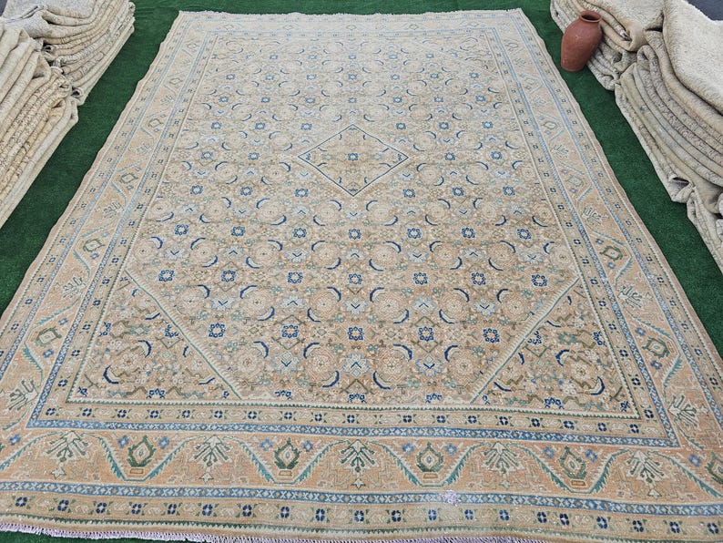 Puede incluir: Una alfombra beige rectangular grande con un intrincado patr&oacute;n de dise&ntilde;os florales y geom&eacute;tricos en tonos de azul, verde y beige. La alfombra tiene un borde detallado y un medall&oacute;n central en forma de diamante. La alfombra es probablemente de lana.