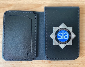 Könnte beinhalten: Schwarzer Leder-Badgehalter mit einem silbernen SIA-Sicherheitsbeamten-Badge. Das Abzeichen hat einen blauen Kreis mit den Buchstaben SIA in Weiß.