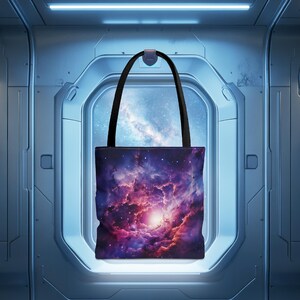 May include: A black tote bag with a galaxy print. The print features a nebula with pink, purple, and blue colors. The bag has black straps.